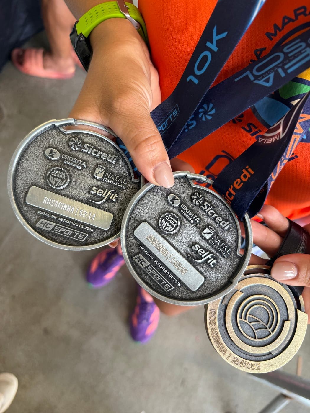 Atleta segurando três medalhas gravadas da Meia Maratona do Sol 2026: 10K, 21K e desafio