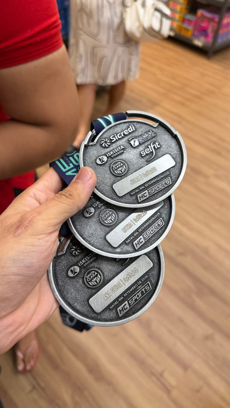 Três medalhas de 10K com nome e tempo gravados na placa, todas no mesmo alinhamento